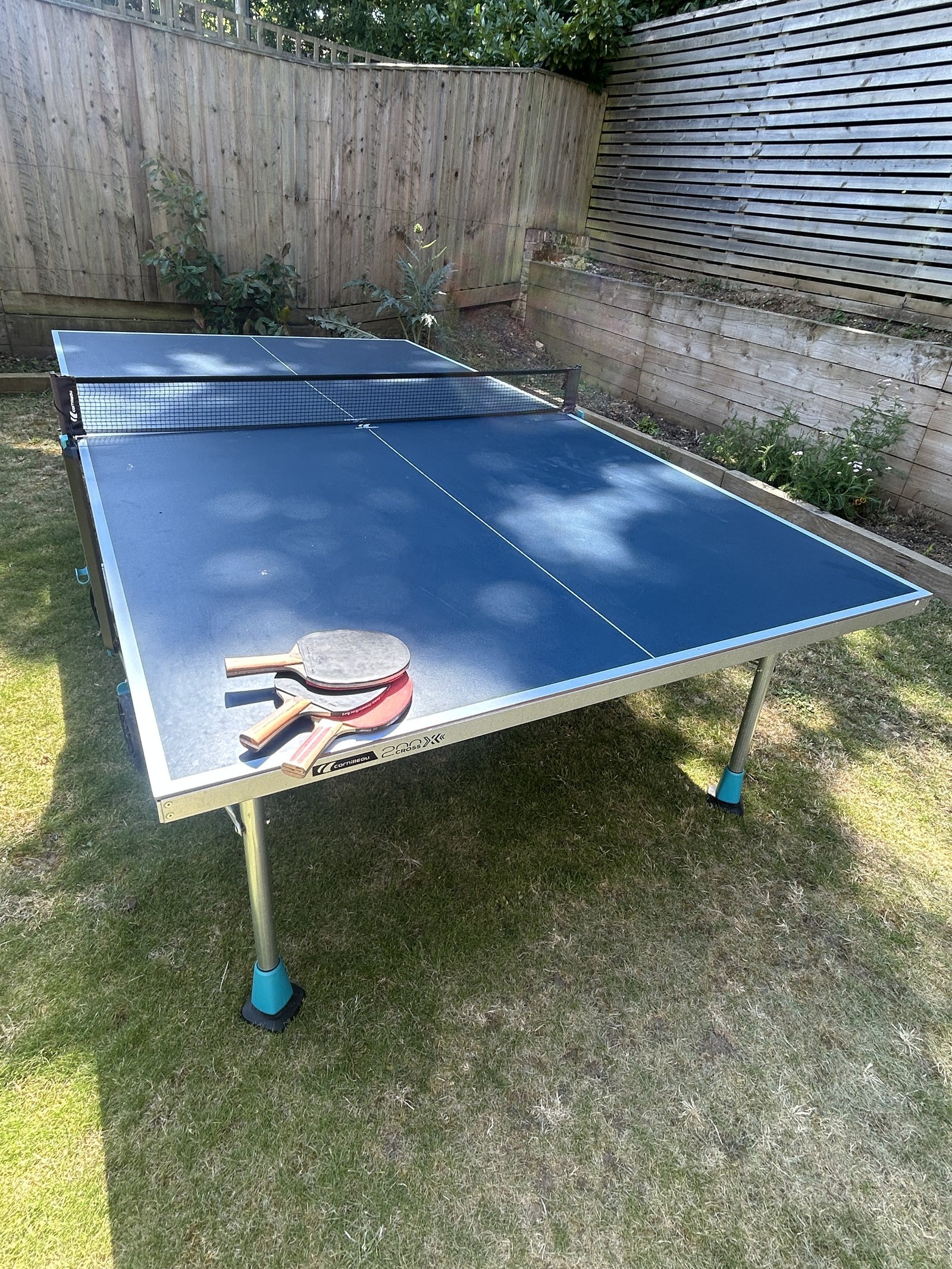 Cornilleau 200X Sport outdoor table tennis table in the garden with bats on top